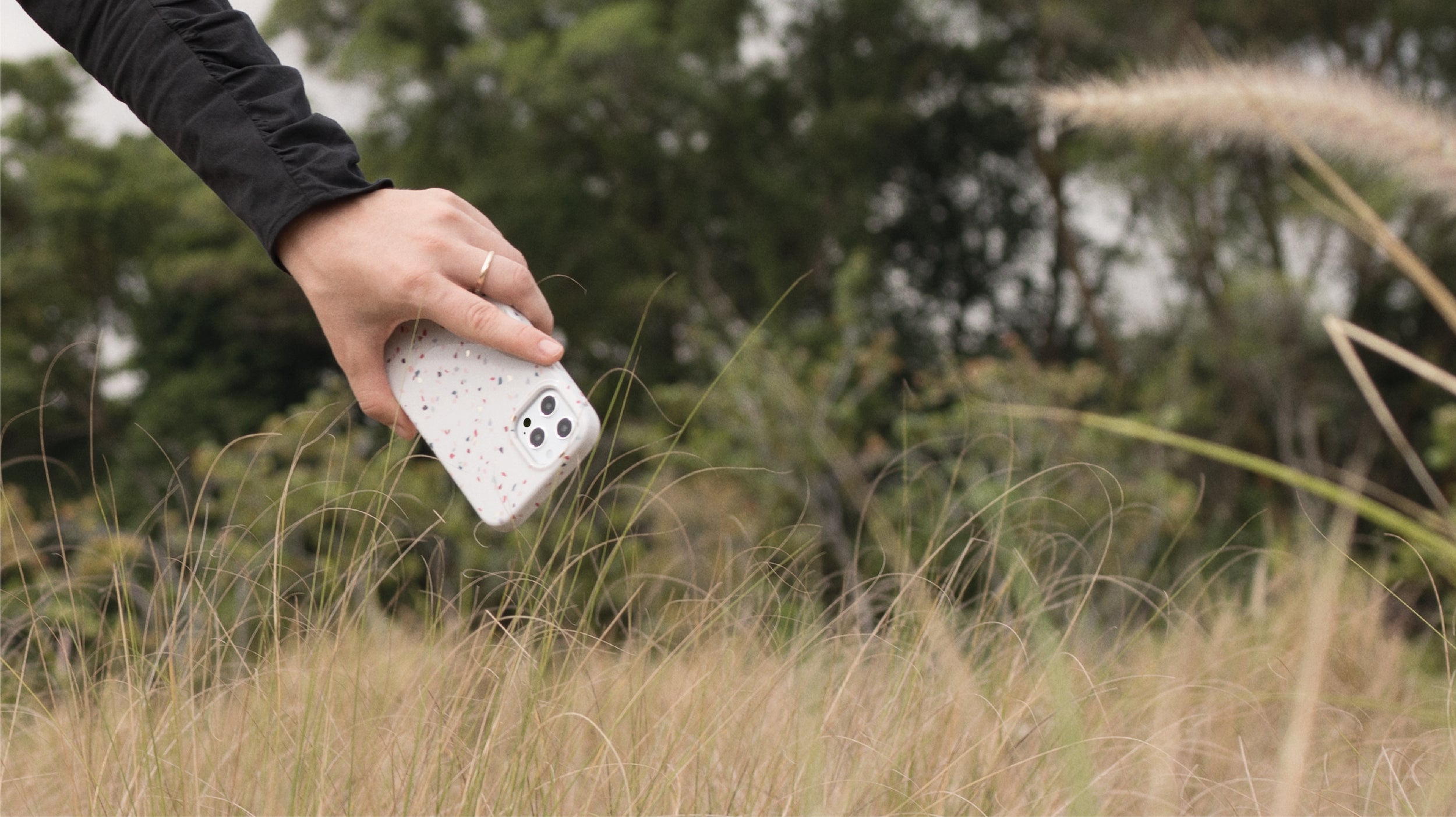 Hand holding speckled phone case in grassy field
