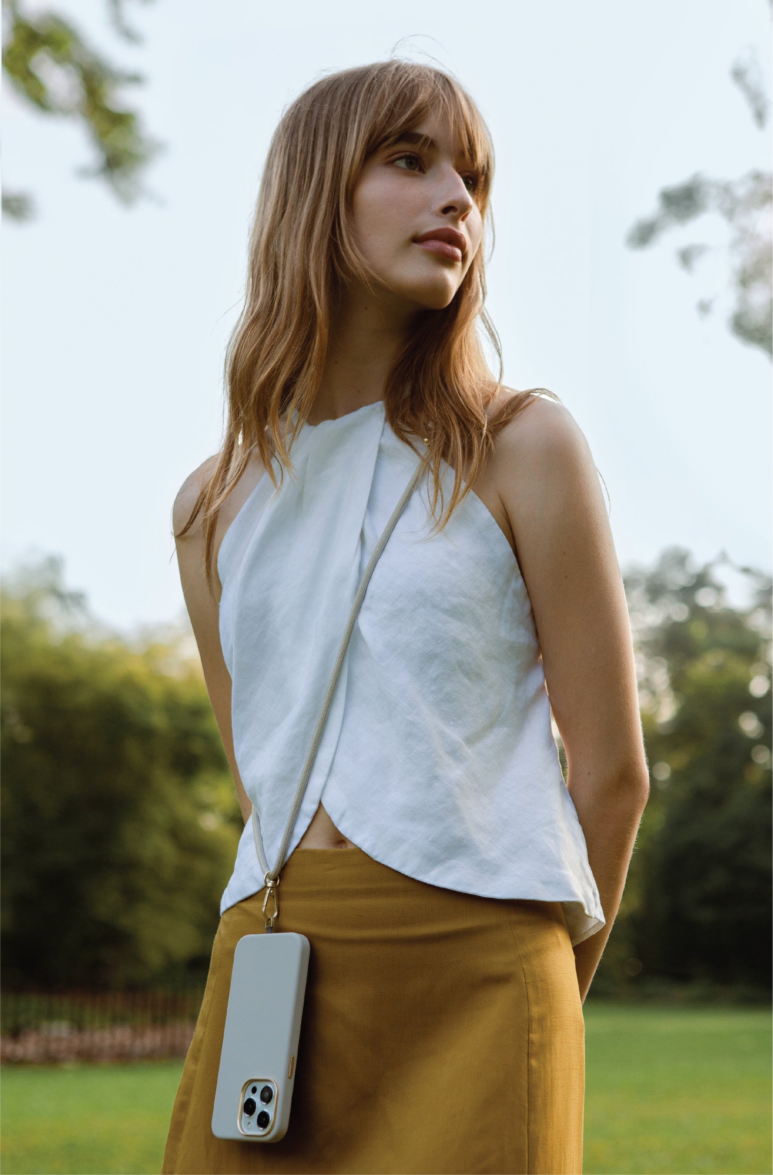 Woman with white top and brown skirt using strap phone case